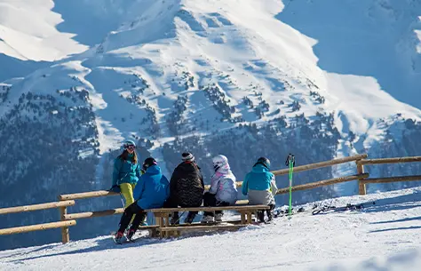 Un groupe d'individus assis sur un banc contemple les montagnes enneigées